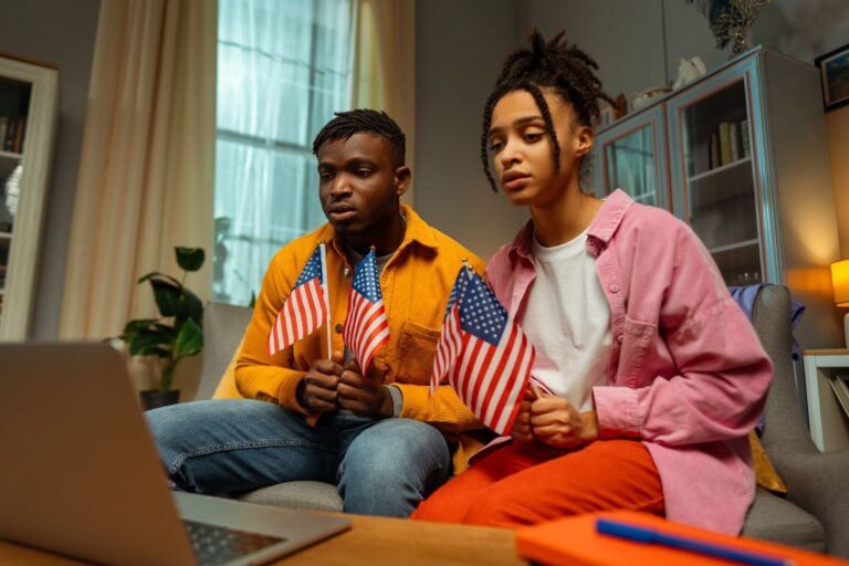 American’s holding a flag looking sad while staring at a laptop