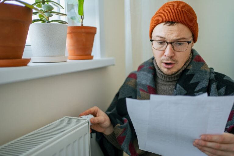 Energy prices increase, man looking at heat bill while wearing a hat and touching the radiator