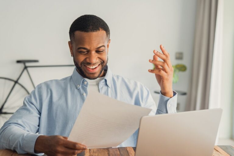 Man happy looking at paperwork at his laptop