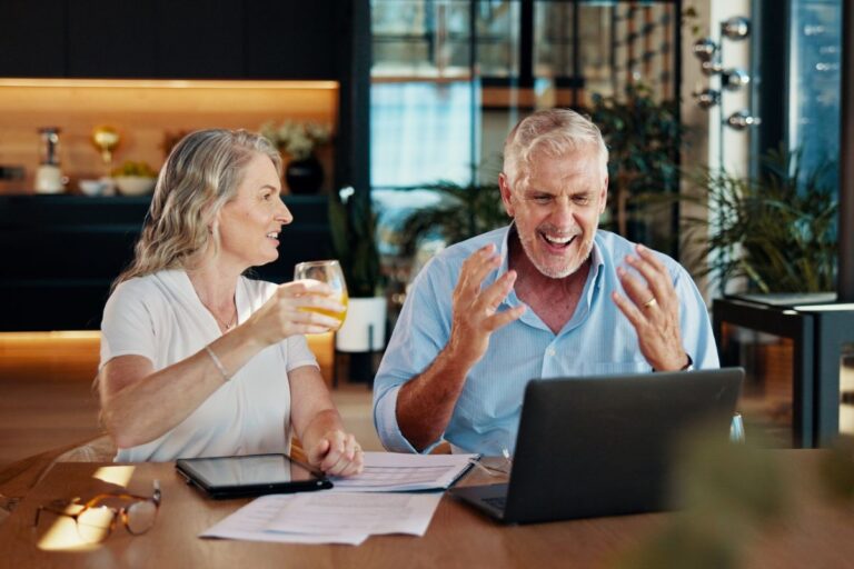Older couple at a bar looking at a laptop happy holding a beer