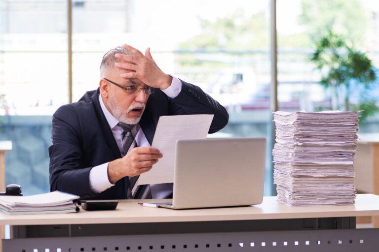 Older man at work looking shocked at paperword