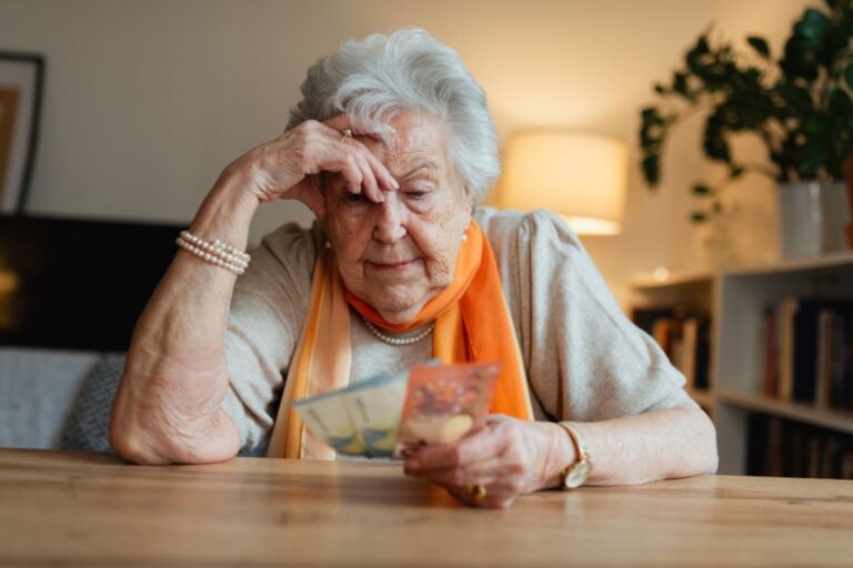 elderly woman looking worried at a table holding money