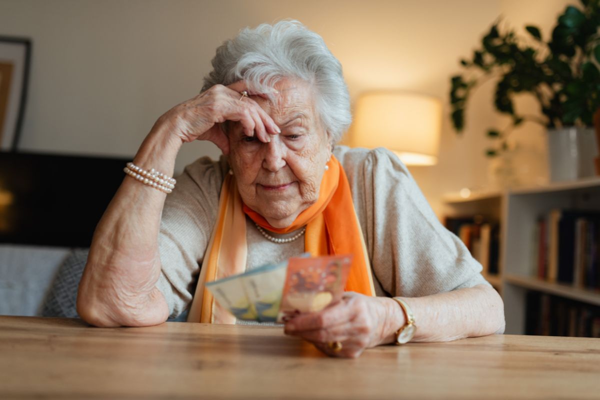 elderly woman looking worried at a table holding money