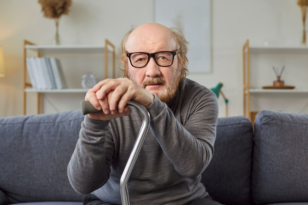 older man sitting on a couch holding a cane