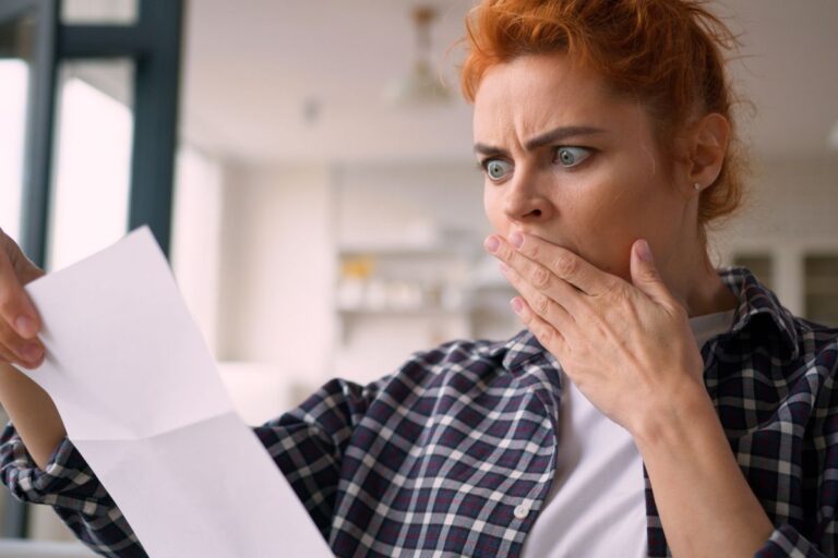 woman with red hair opening a letter shocked holding her mouth