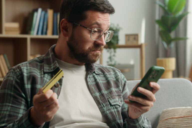 Man looking at his phone holding his bank card looking surprised