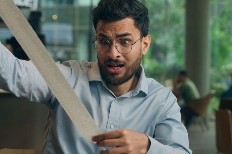 Man with glasses looking shocked holding a long receipt