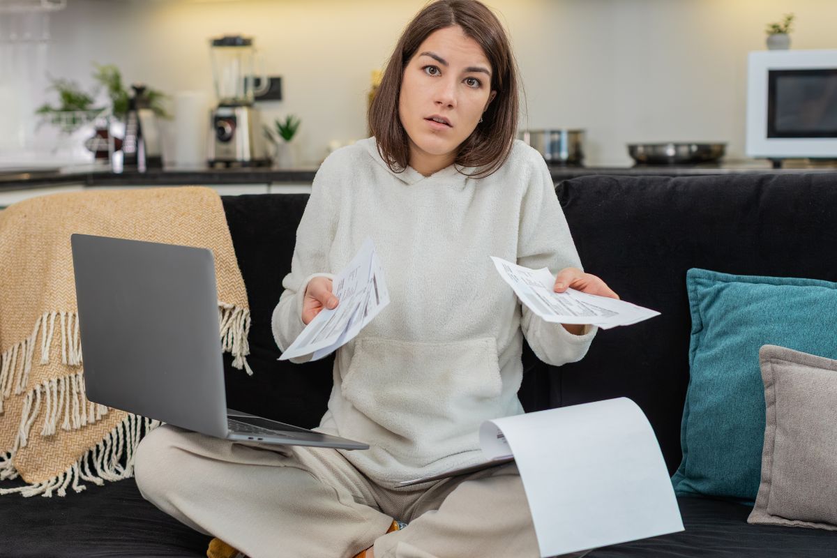 Woman holding bills and her laptop with her shoulders shrugged