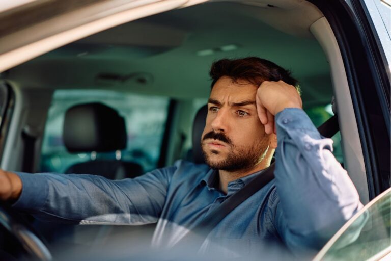 man driving to work hand on his head as if stuck in traffic
