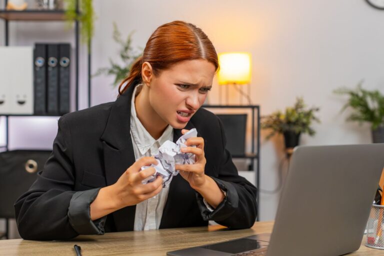woman at work crumpling paper in anger infront of a laptop