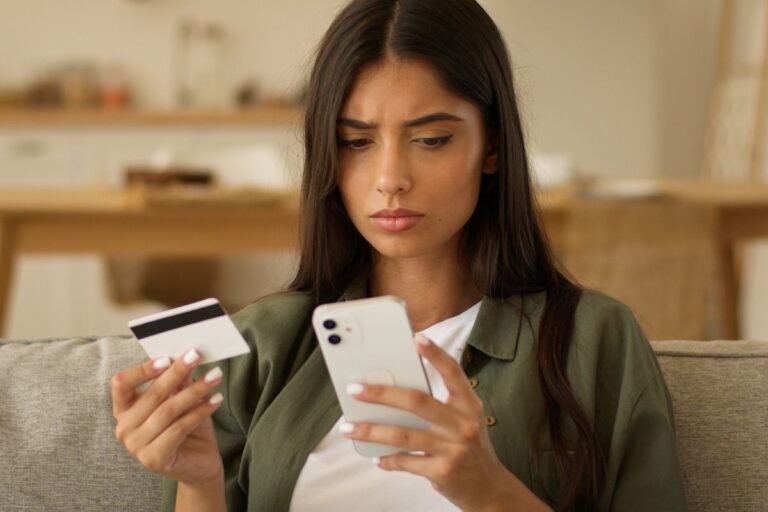 woman looking at her phone while holding a credit card