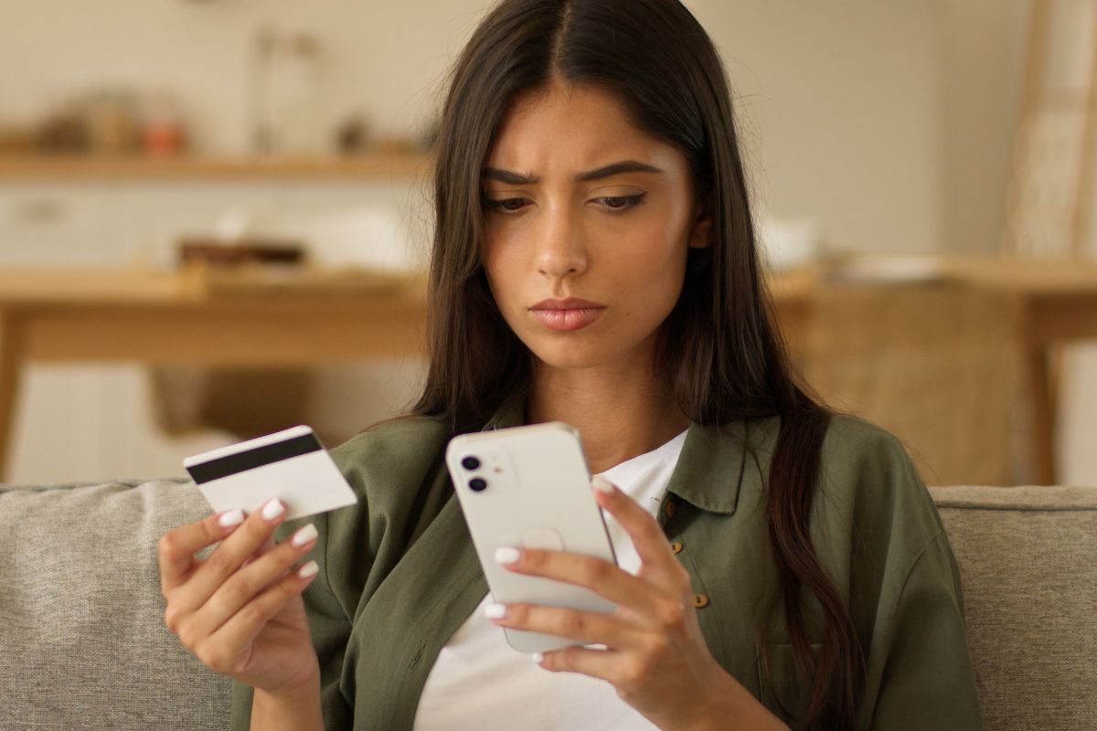 woman looking at her phone while holding a credit card