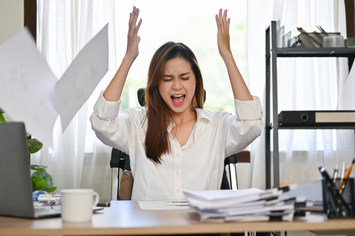 woman throwing paper and hands in the air out of frustration at a desk