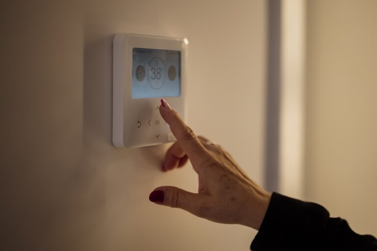 A hand adjusting the temperature on a wall thermostat inside a home