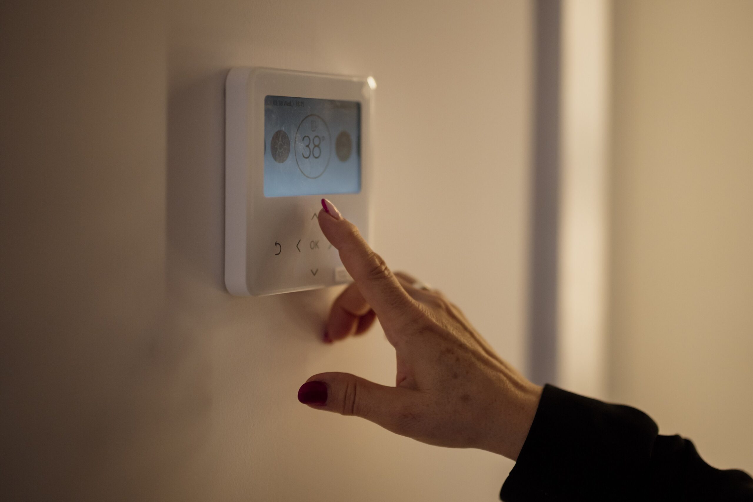 A hand adjusting the temperature on a wall thermostat inside a home
