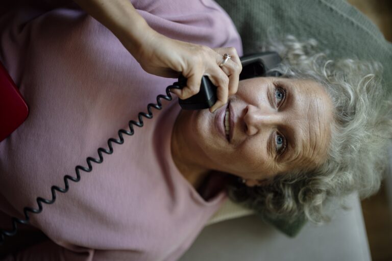 An older woman talking on a landline phone while resting on a couch at home
