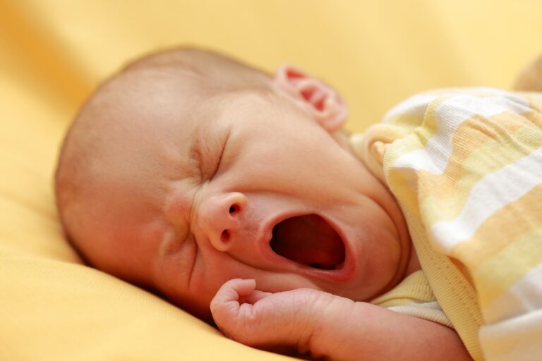 A yawning newborn infant wrapped in a blanket
